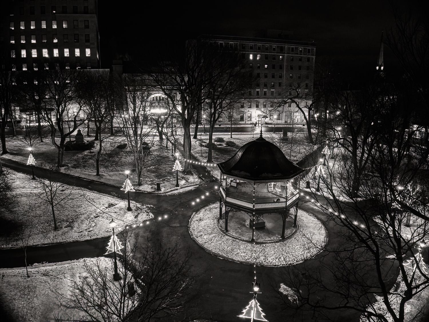 A snowy winter night scene in a city park with illuminated paths and a gazebo creating a peaceful atmosphere, Kings square, Saint John, NB