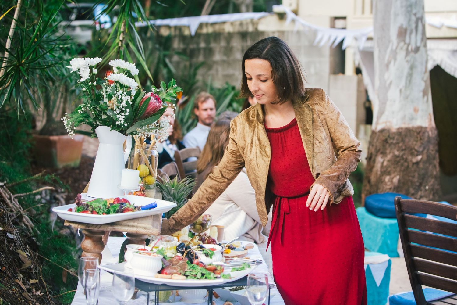 Guests enjoying a festive outdoor garden party with food and drinks on decorated tables.