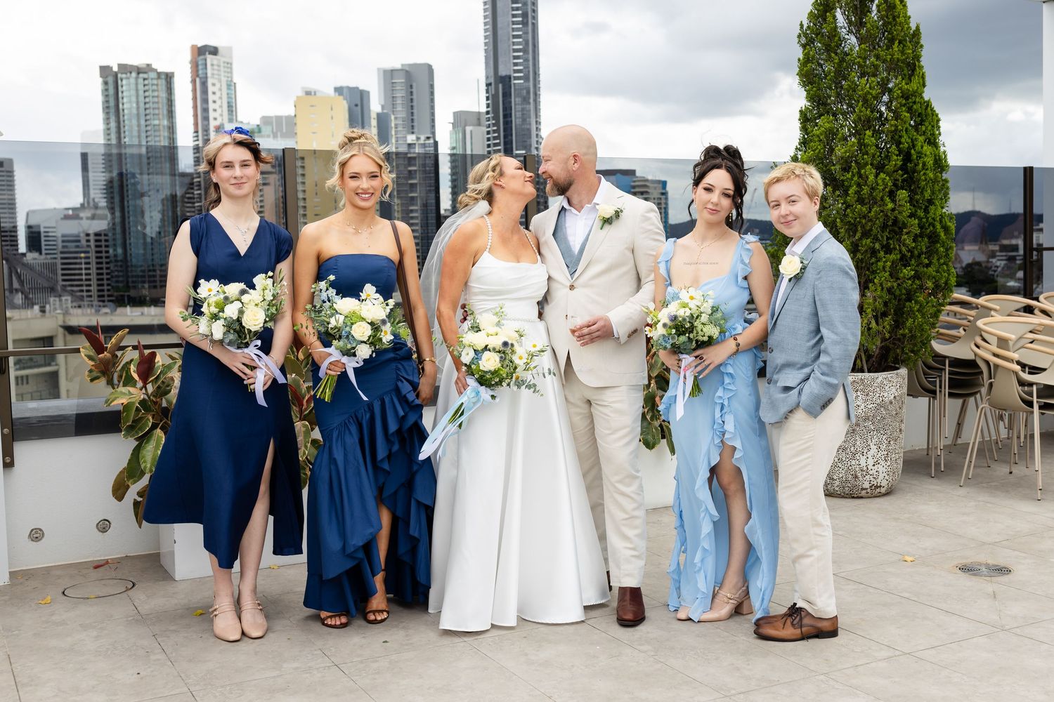 Wedding party poses together in front of modern city skyline on a bright sunny day.