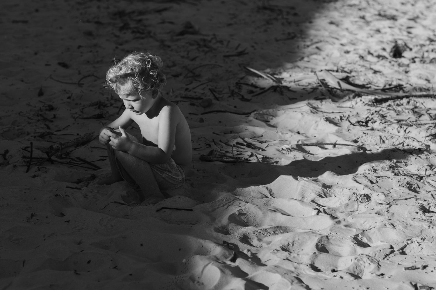 Footprints in black and white sand leading along a beach shoreline.Family photography Kirra beach Gold Coast