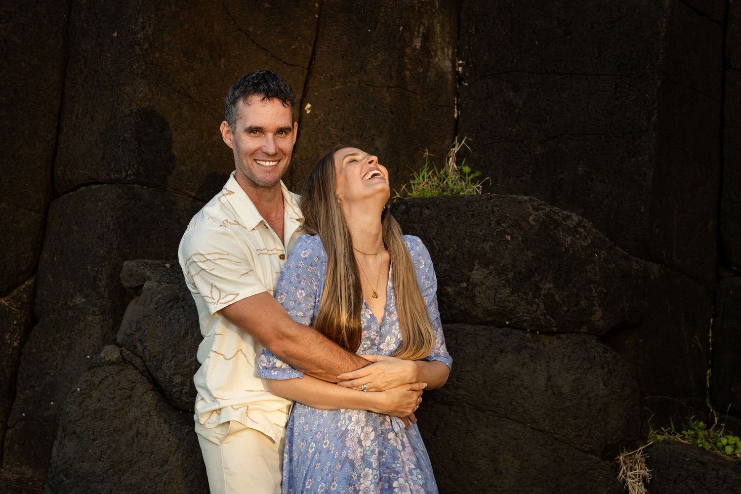 Two people share joyful laughter while dancing together against a dark rocky backdrop.Fingal head family photos -  New South Wales