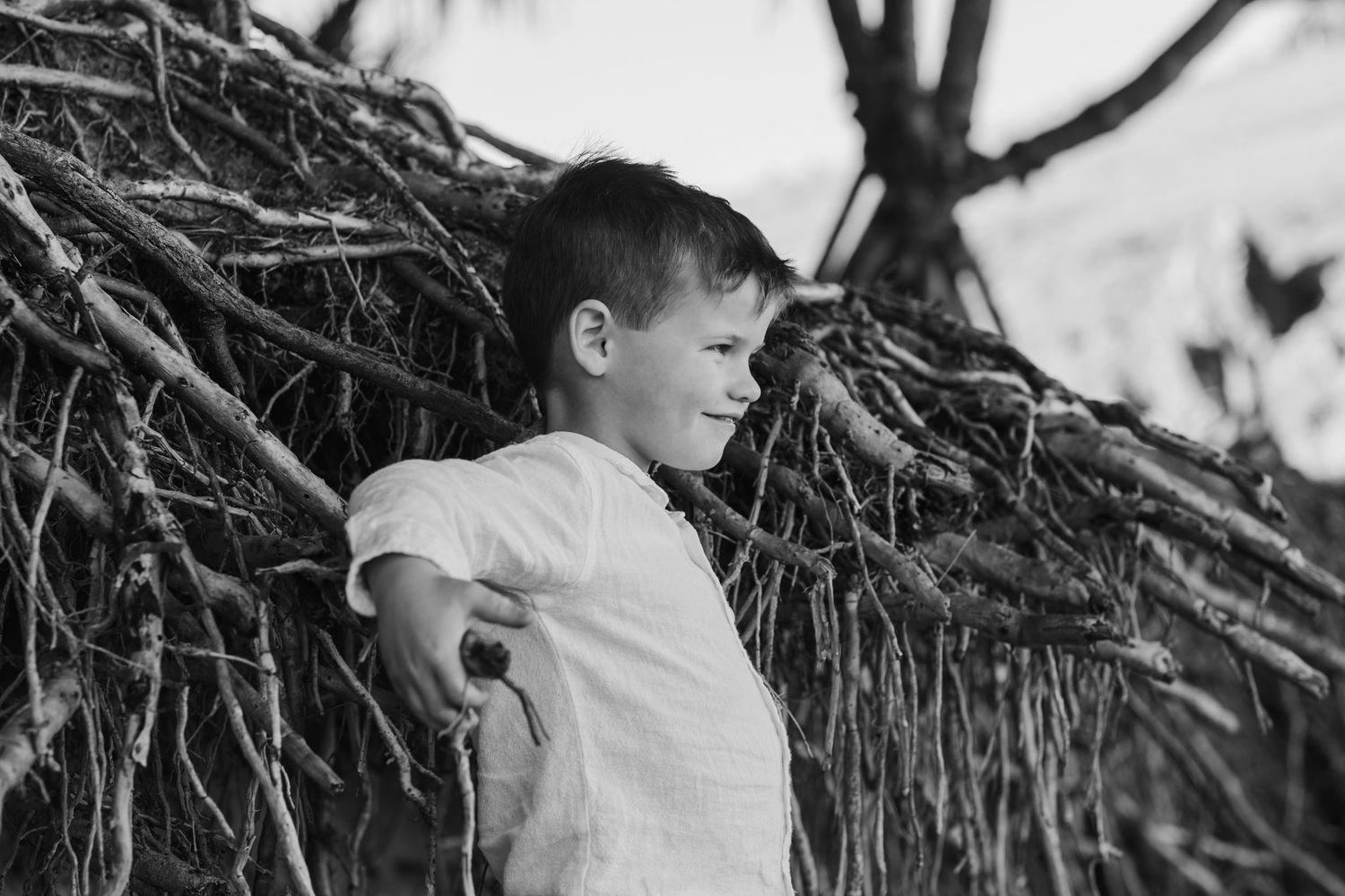 Child in white shirt stands against textured branch background in monochrome.Cabarita headland