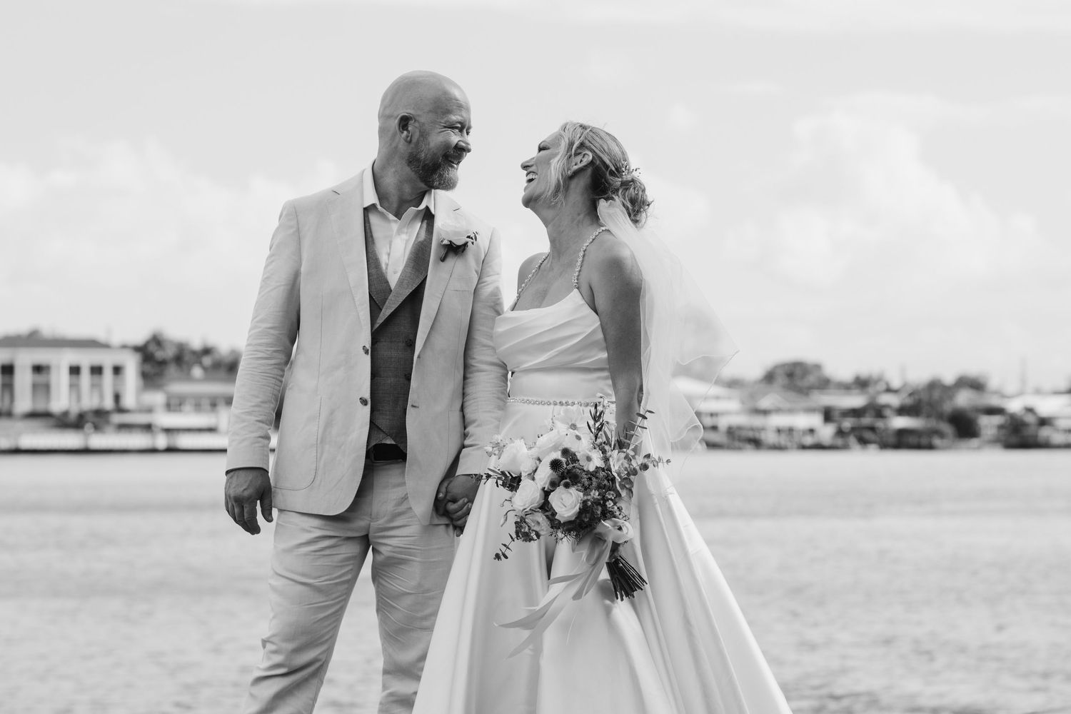 Couple shares romantic moment on waterfront with cityscape in background.New farm park wedding photos in Brisbane