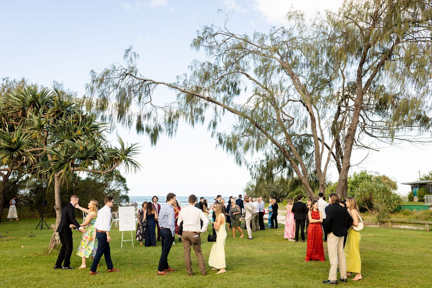 Wedding celebration taking place under large trees in a scenic outdoor setting.beach wedding currumbin surf club wedding