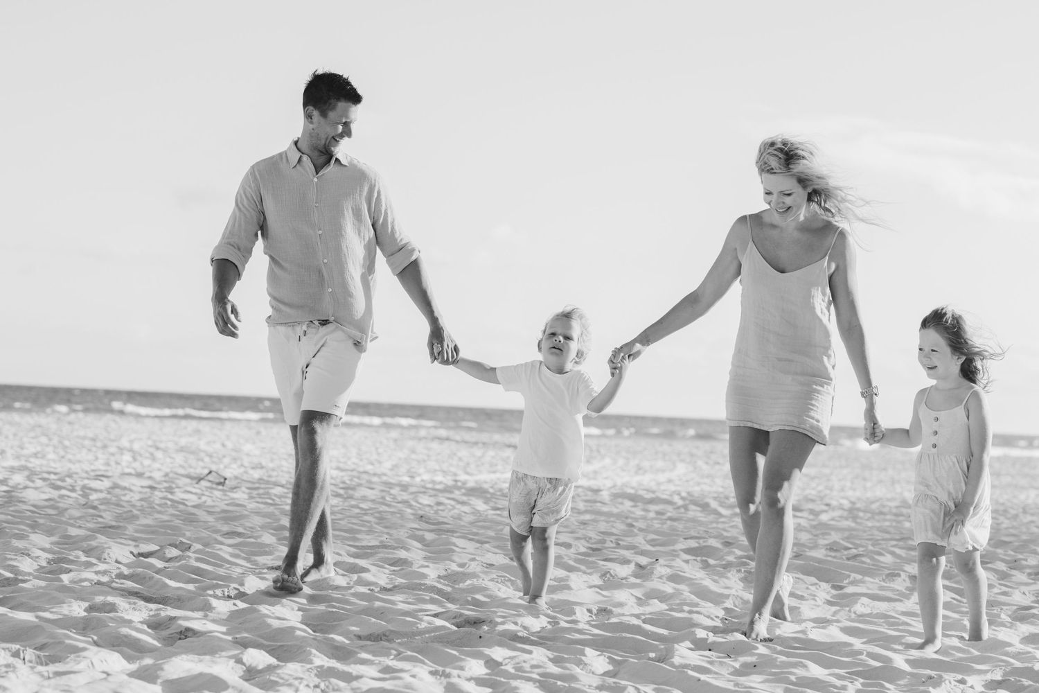 Family walking together hand in hand along the shoreline.Gold Coast candid family photographer.