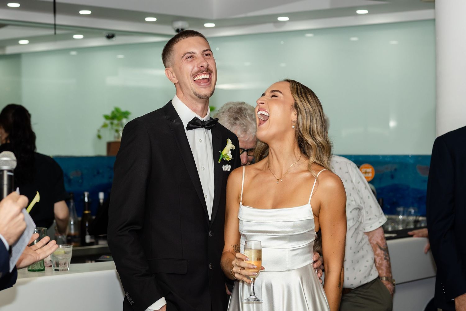 Wedding guests laugh and celebrate during a joyful reception party in an indoor venue.beach wedding currumbin surf club wedding
