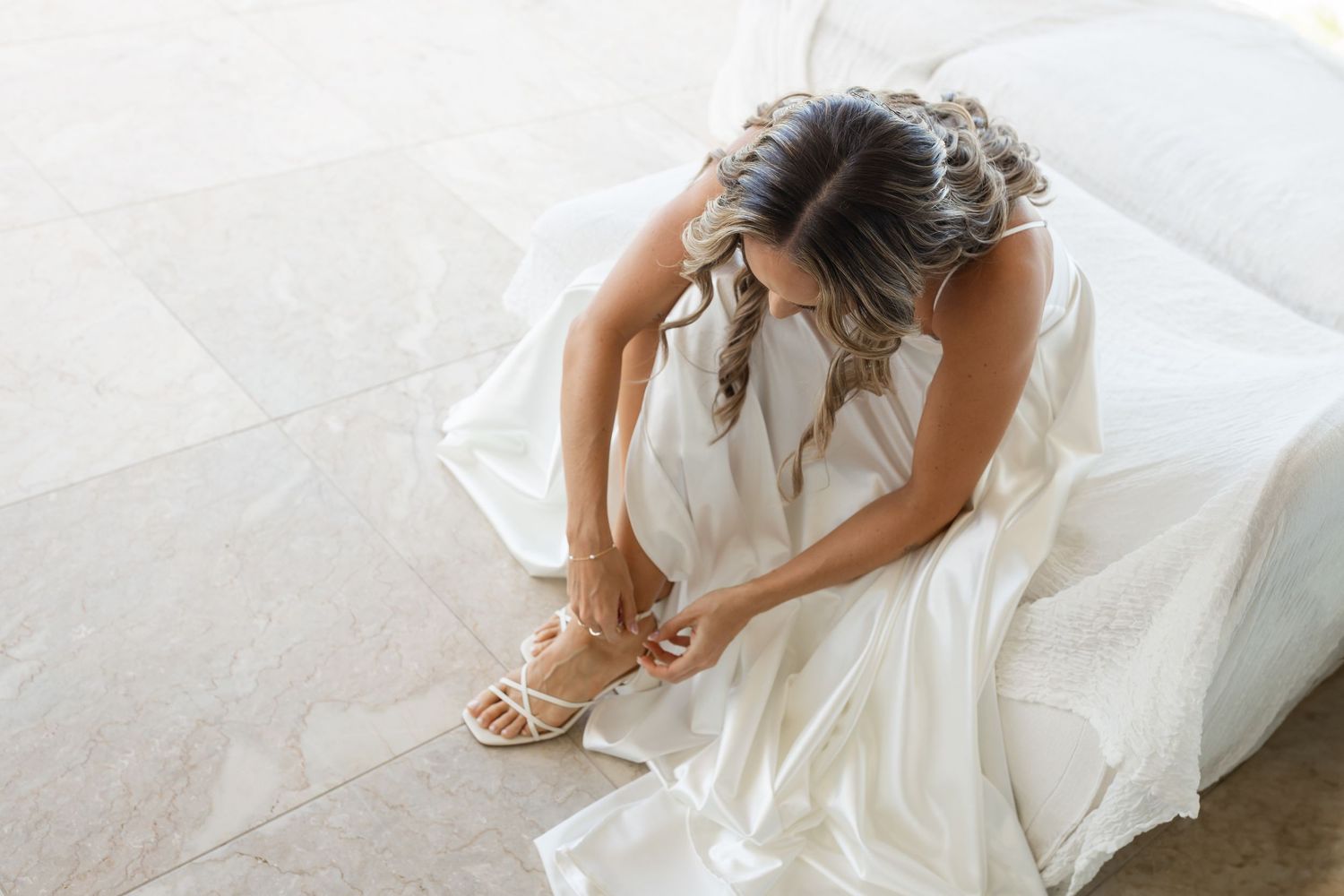 A bride in a flowing white wedding dress sits elegantly on a cushioned surface.beach wedding currumbin surf club wedding