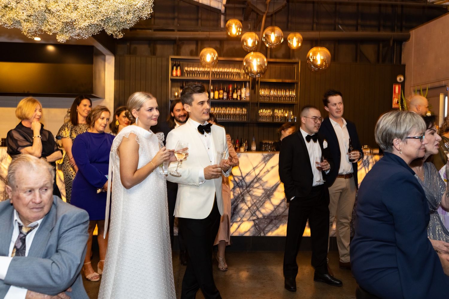 Wedding reception venue decorated with hanging lights and filled with celebrating guests.