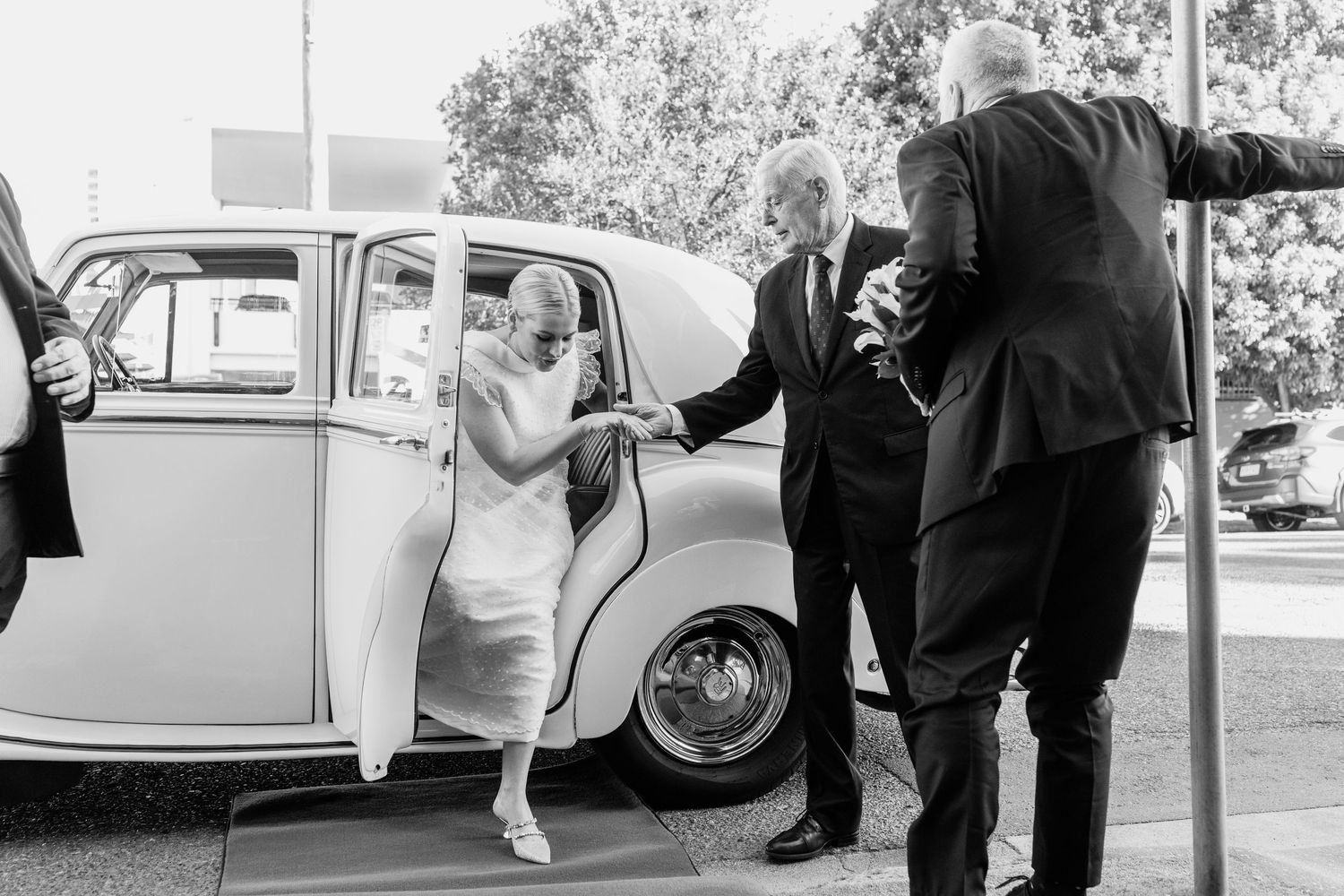 Vintage car arrives at outdoor wedding ceremony with guests gathering around.