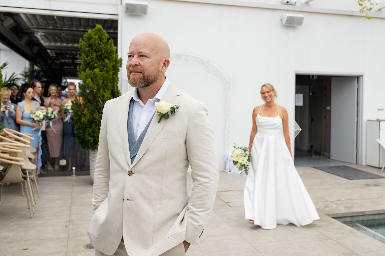 Wedding party members in light colored formal attire gathered outdoors.