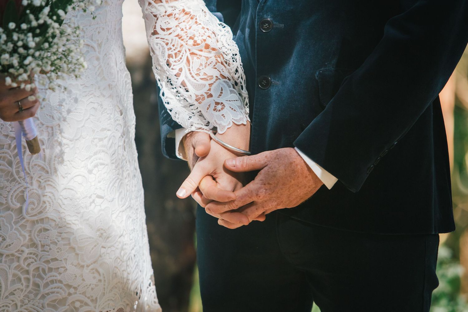 Close-up details of lace wedding dress and hands during ceremony.