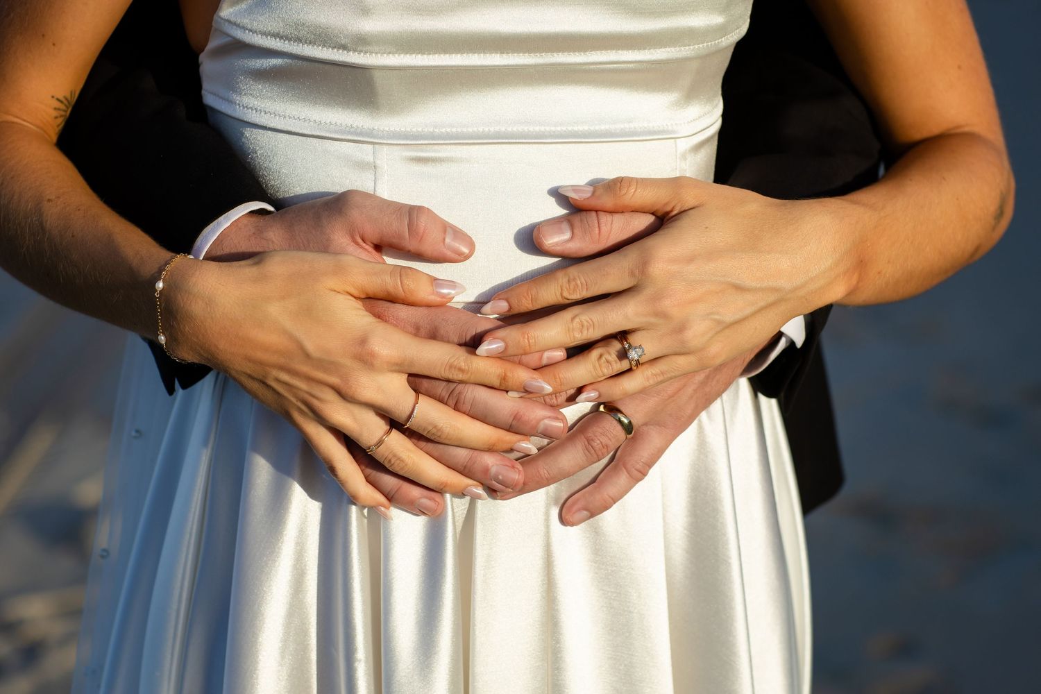Close-up of hands embracing around white dress waist showing wedding rings.beach wedding currumbin surf club wedding