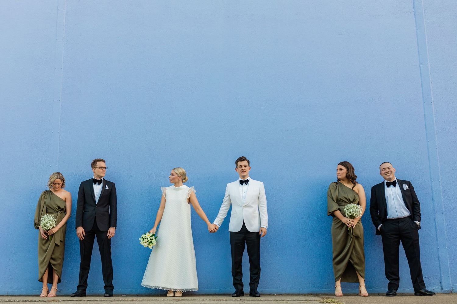 Wedding couple and wedding party pose against bright blue wall for creative portraits.