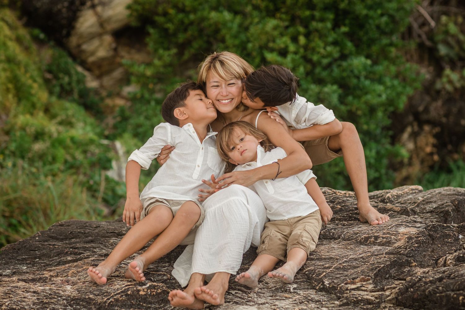 Family relaxes together on fallen tree trunk in lush green forest setting. Gold Coast candid family photographer.