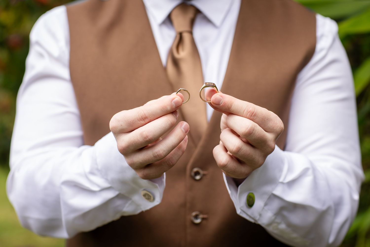 Hands hold wedding rings against a brown vest and white shirt background.Gold Coast hinterland wedding photographer