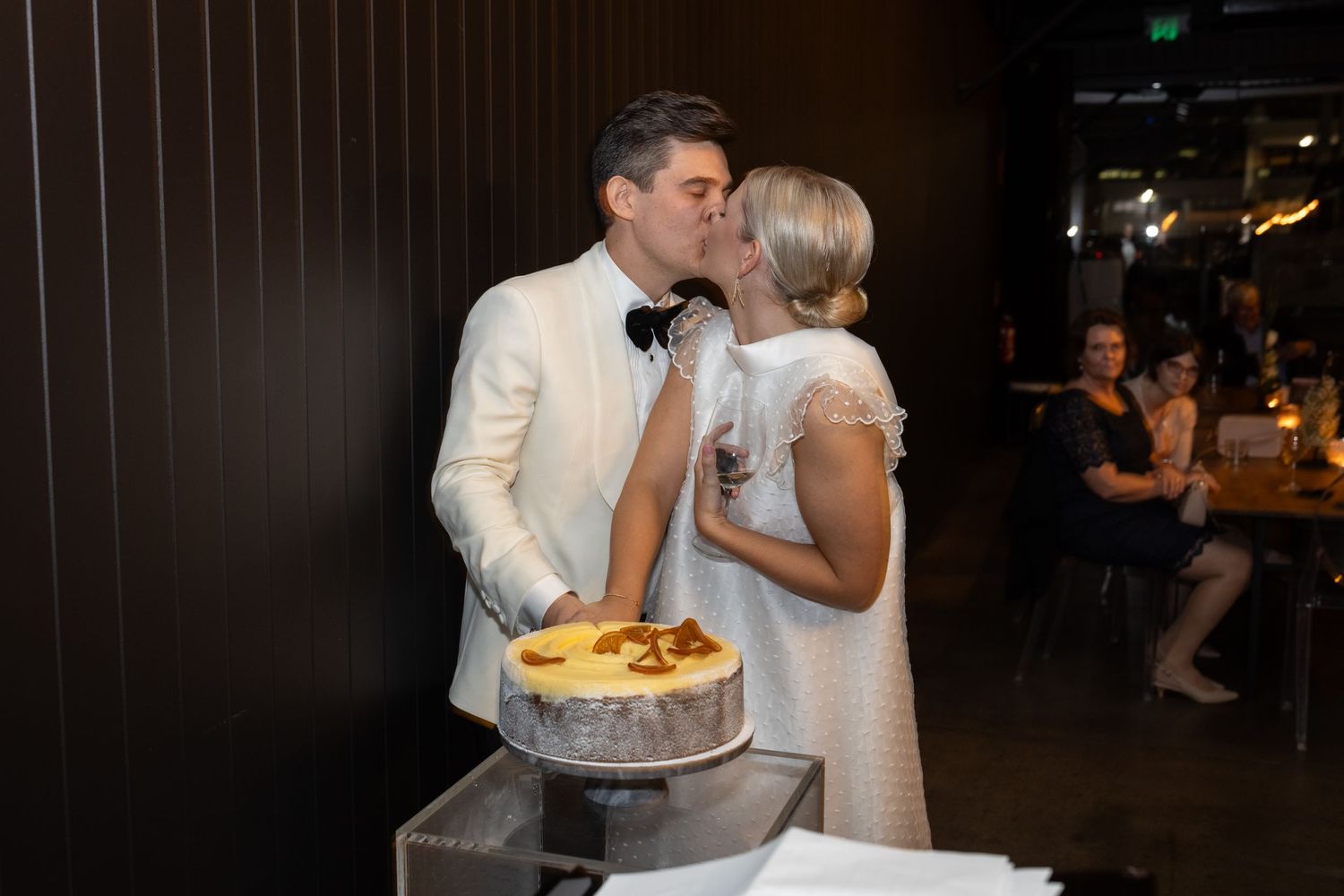 Wedding reception moments with cake cutting and dancing in warm ambient lighting.
