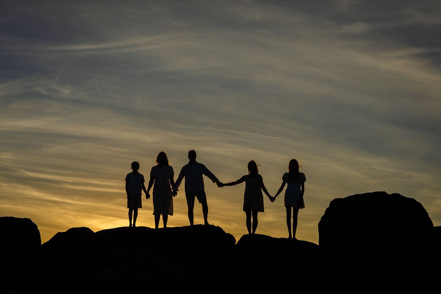 Silhouettes of people standing on a ridge against a dramatic sunset sky.Gold Coast candid family photographer. Gold Coast candid family phot