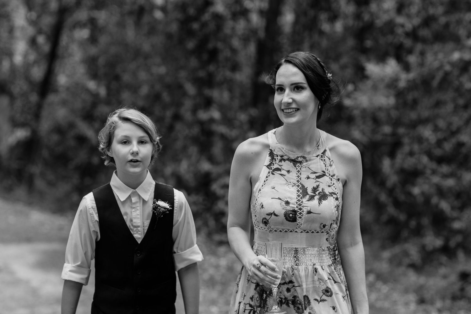 A black and white photo captures a tender moment between two people in a forest setting.