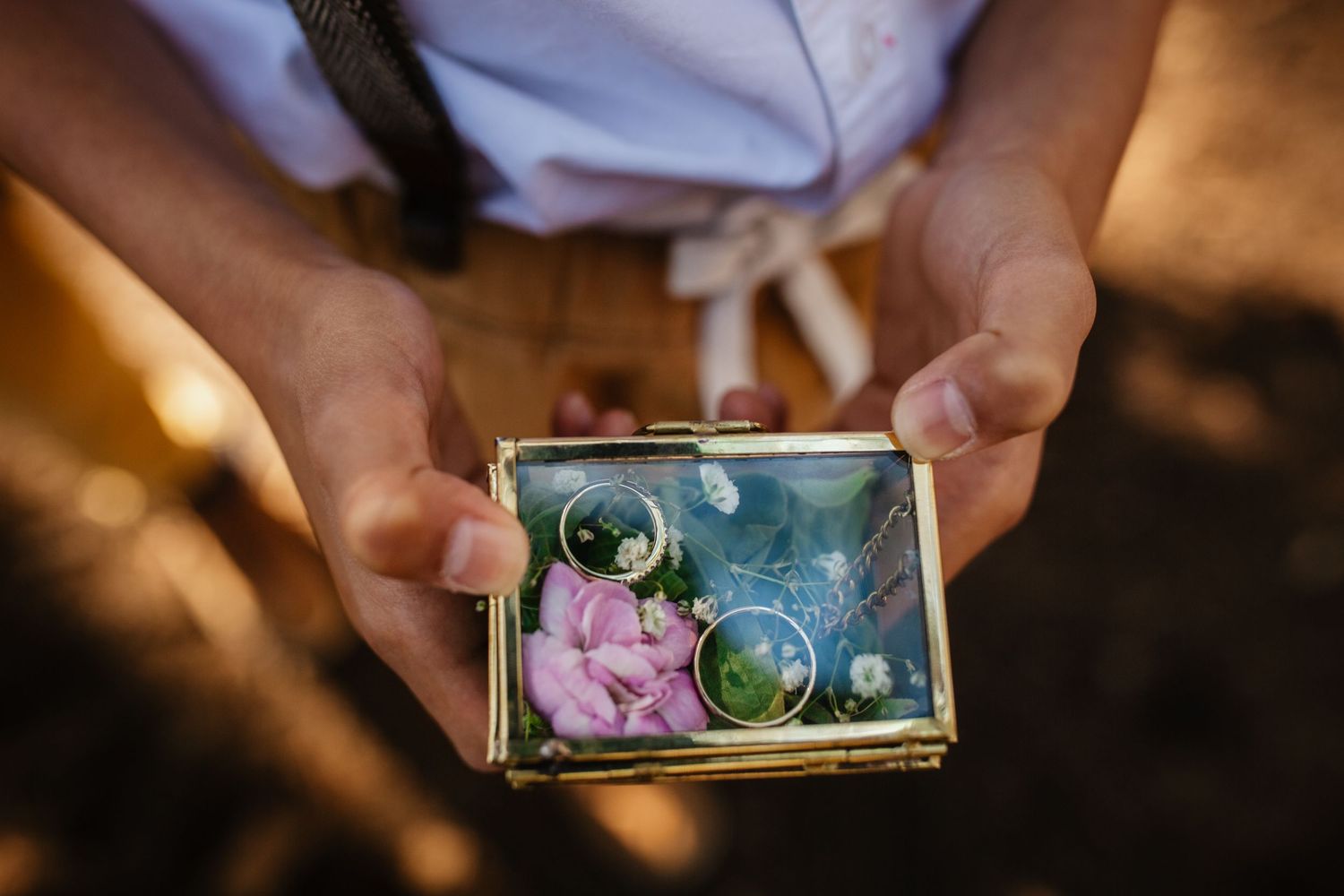 A delicate ring box holds pink flowers and wedding rings in a close-up detail shot.
