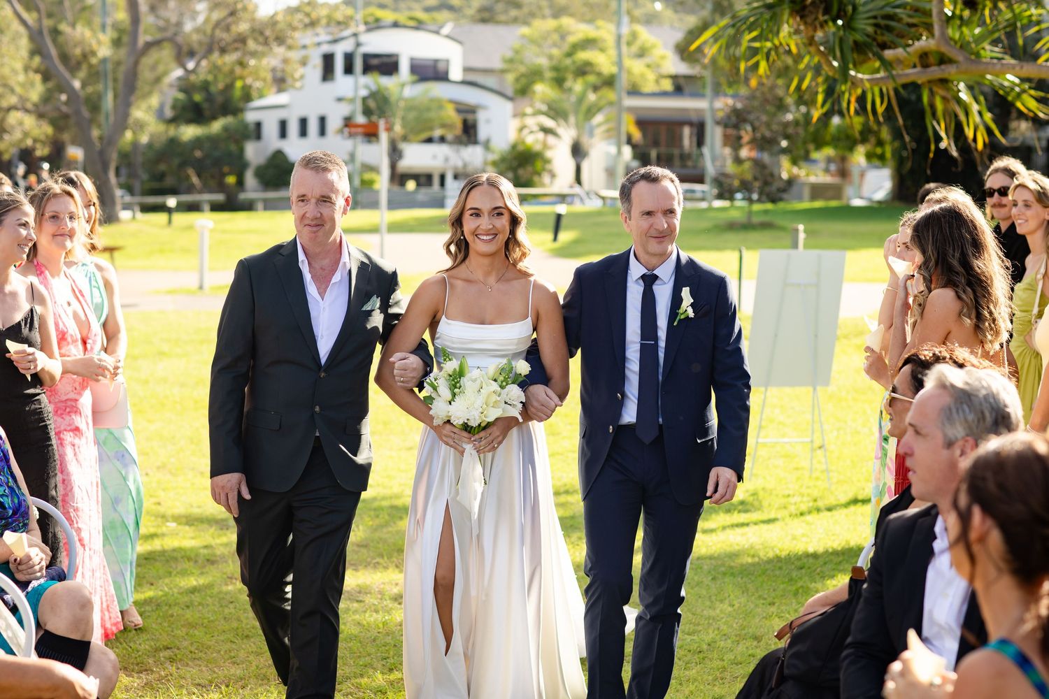 Wedding party members walk together during outdoor ceremony in formal attire.