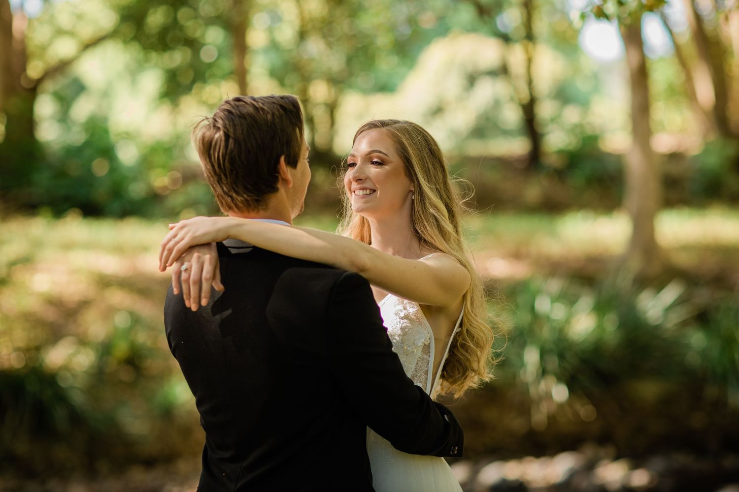 A romantic outdoor wedding moment captured in a wooded setting with natural sunlight.
