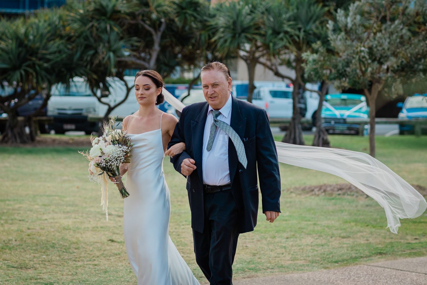 Wedding couple walking through landscaped garden path during outdoor celebration.