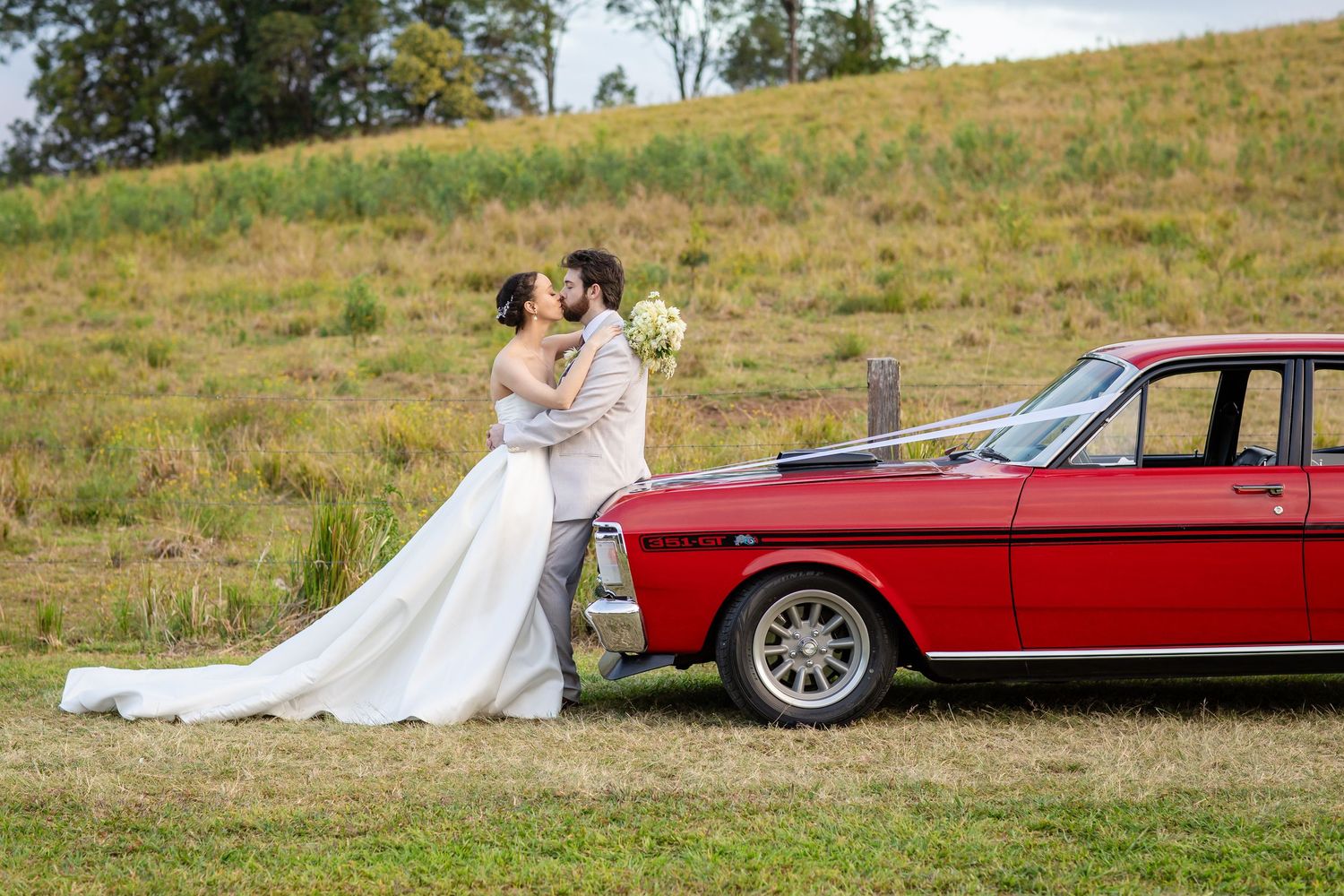 A classic red car parked in a grassy field during a wedding photoshoot.The barrow restaurant mount Nathan wedding