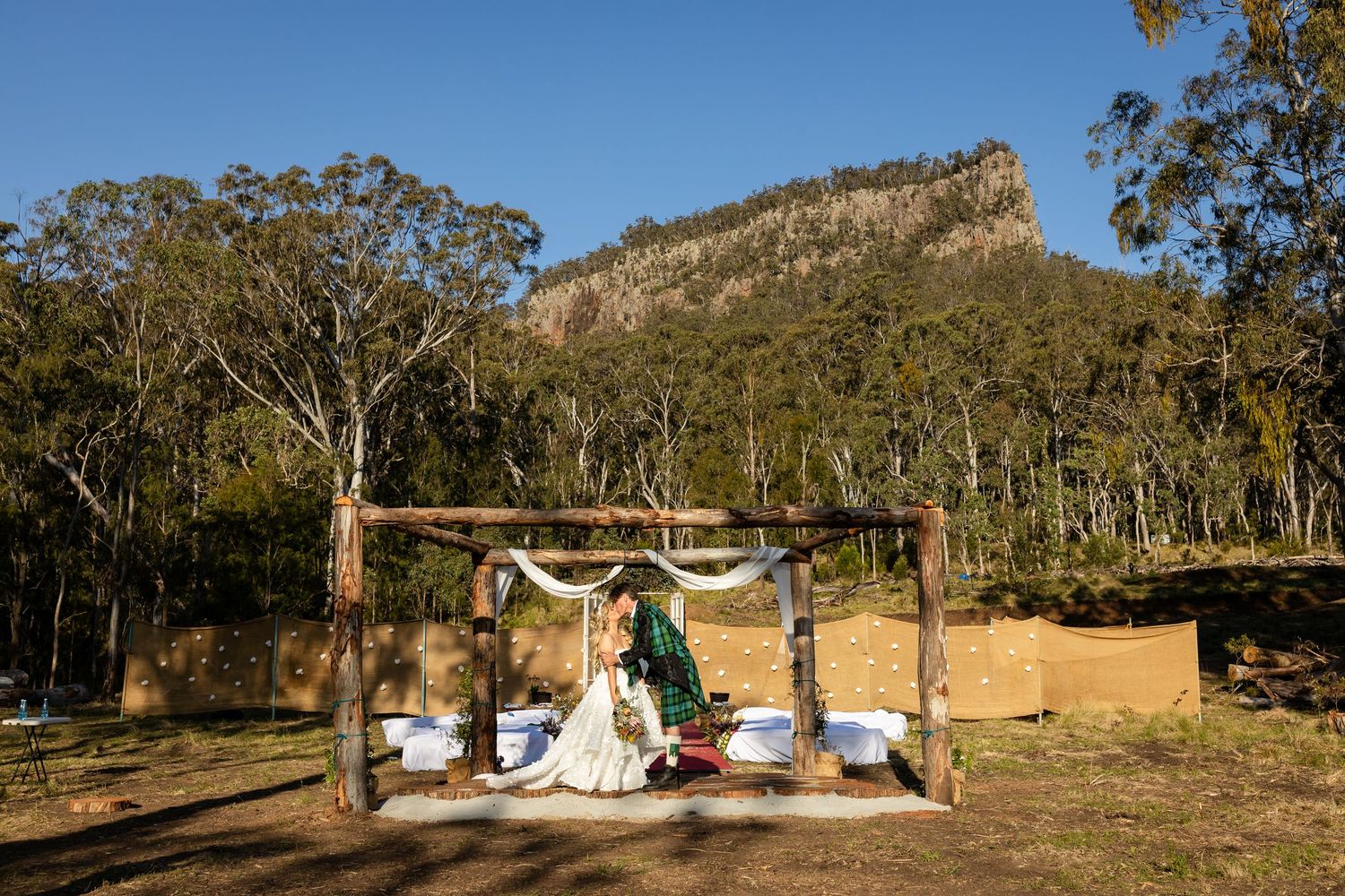 Wedding ceremony setup with wooden arch against dramatic mountain backdrop in Australian bushland setting.Gold Coast wedding photographer