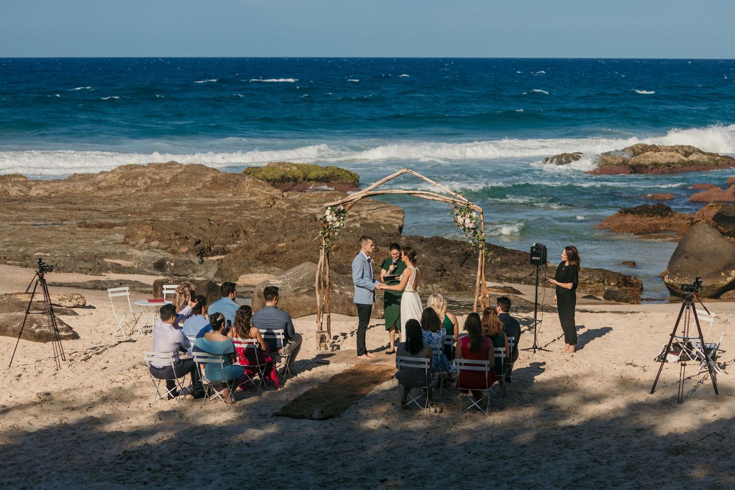 Wedding guests seated on beach chairs watching oceanside ceremony.