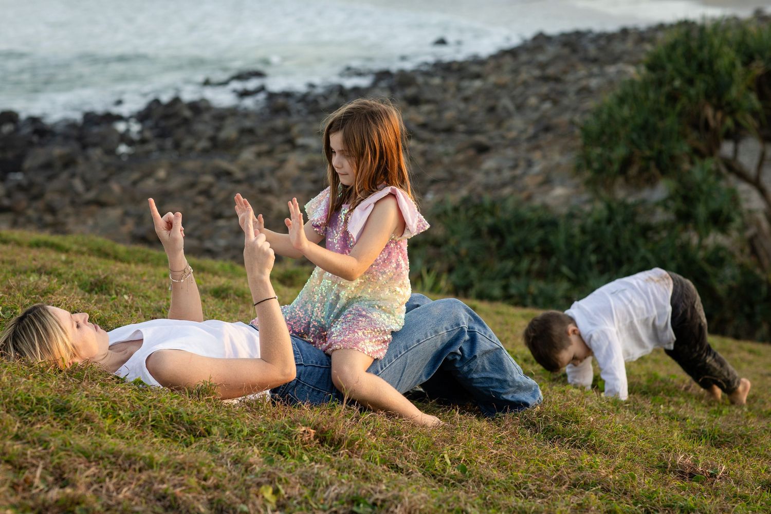 People lounging on grassy slope near rocky coastline.Gold Coast candid family photographer. Cabarita headland