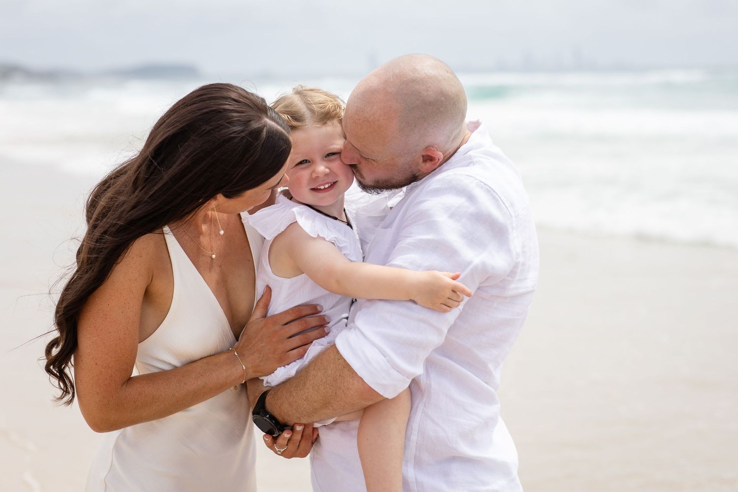 A joyful family moment captured on the beach with everyone dressed in white sharing laughter and embraces.