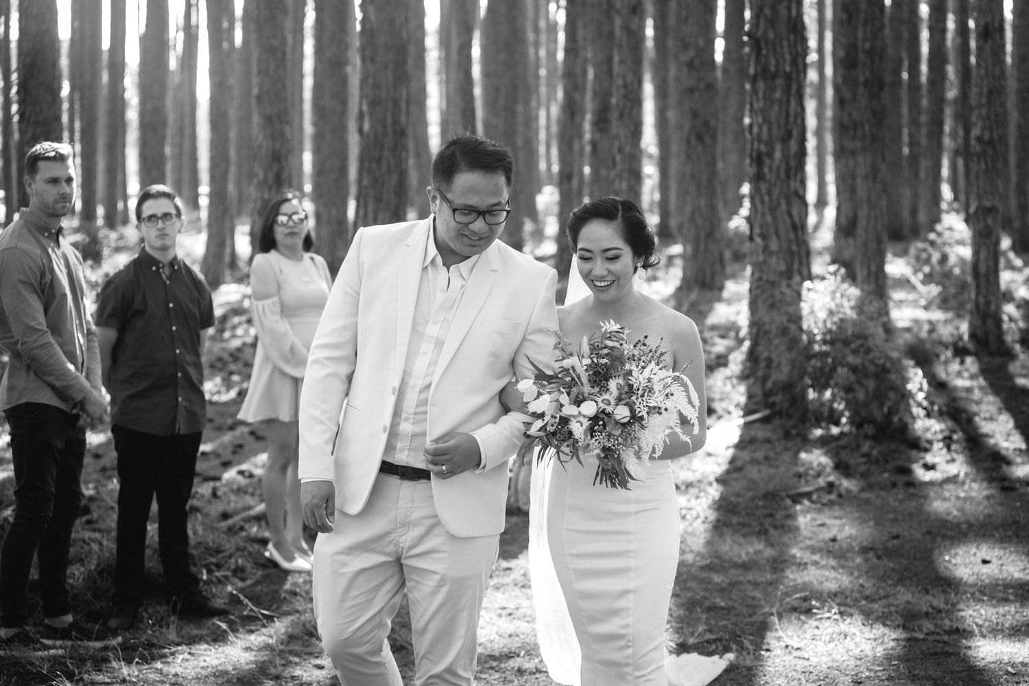 Wedding ceremony in a sunlit forest with tall trees creating a magical woodland setting.