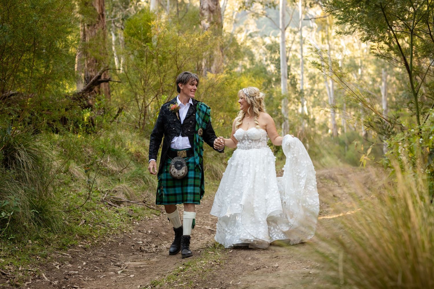 Couple walking along bush trail with groom in traditional kilt and bride in flowing white dress.Gold Coast wedding photographer