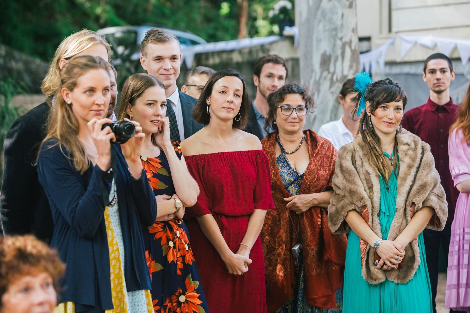 Wedding guests gather outdoors in colorful attire for a celebration.