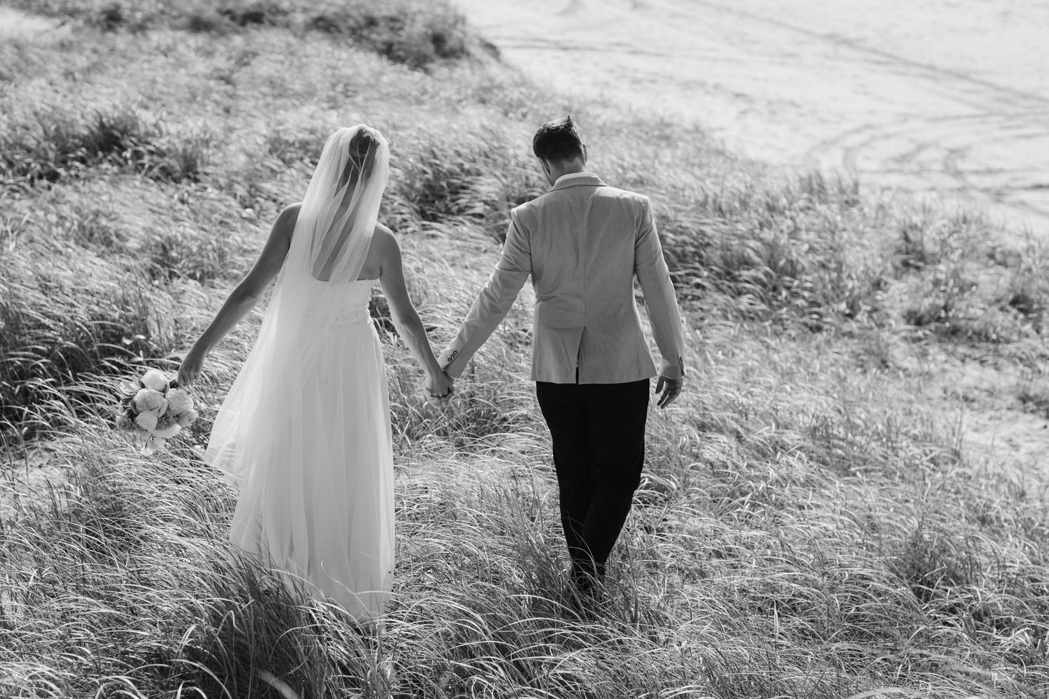 Black and white portrait of couple walking together on grassy hillside.