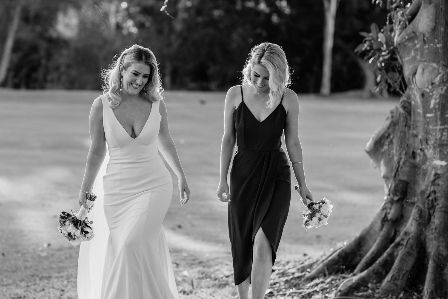 Two people in contrasting formal dresses walking together holding bouquets. Surfers Paradise Golf Club wedding.