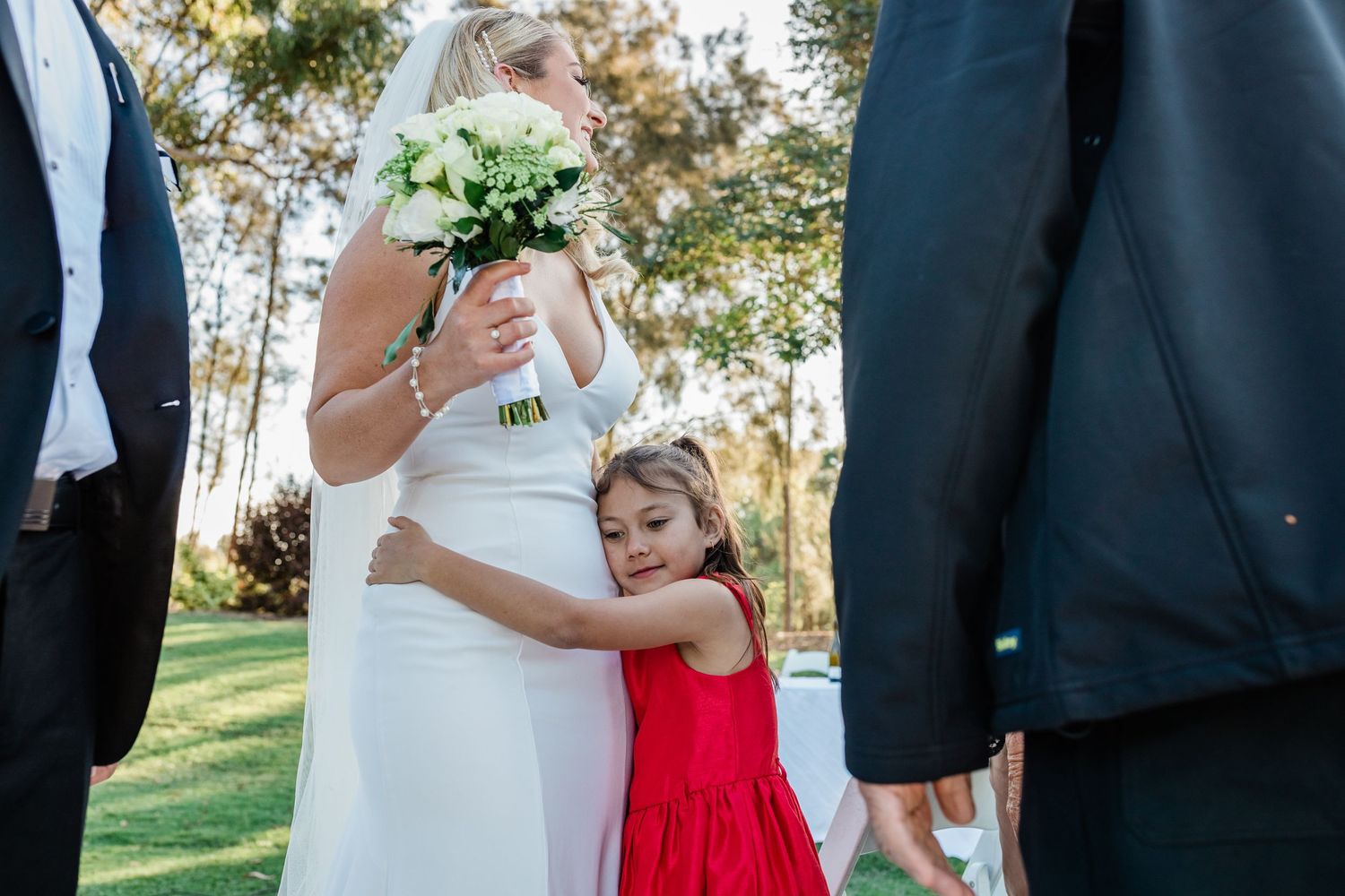 Wedding party members share candid moments and laughter during outdoor photo session in a garden setting.
