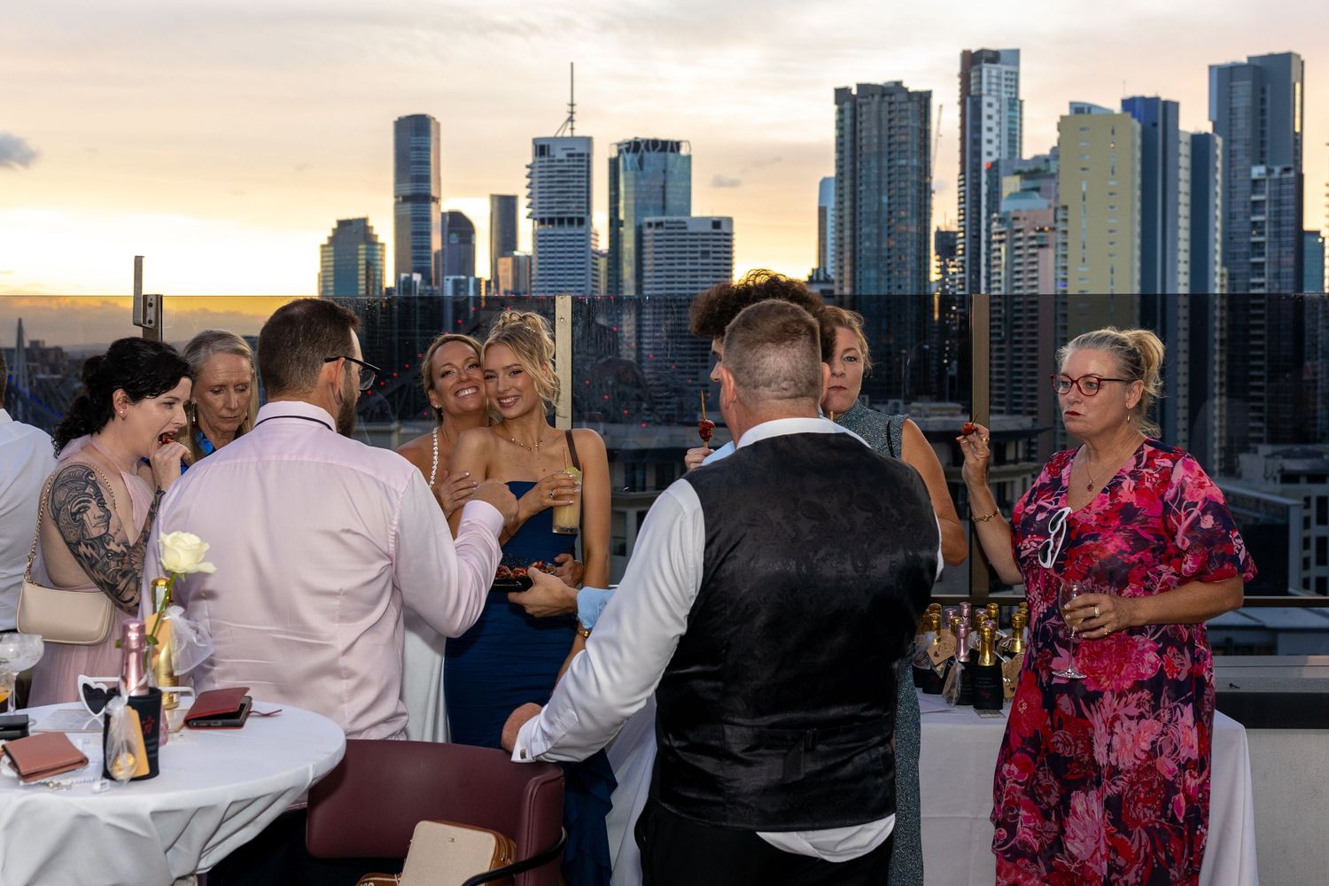 Wedding guests celebrate on a rooftop venue with  brisbane city skyline visible at sunset.