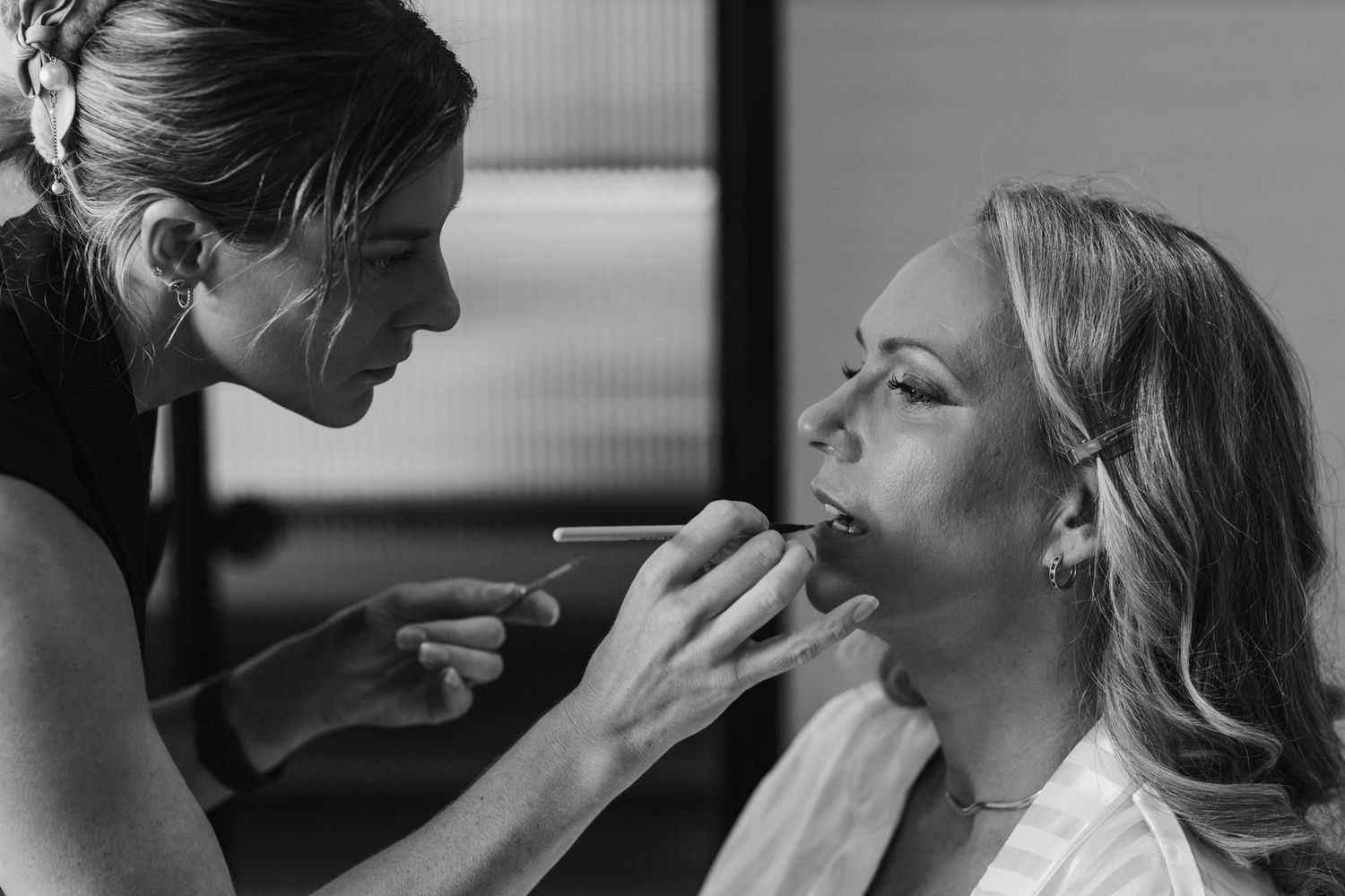 Black and white image showing wedding makeup application in progress.
