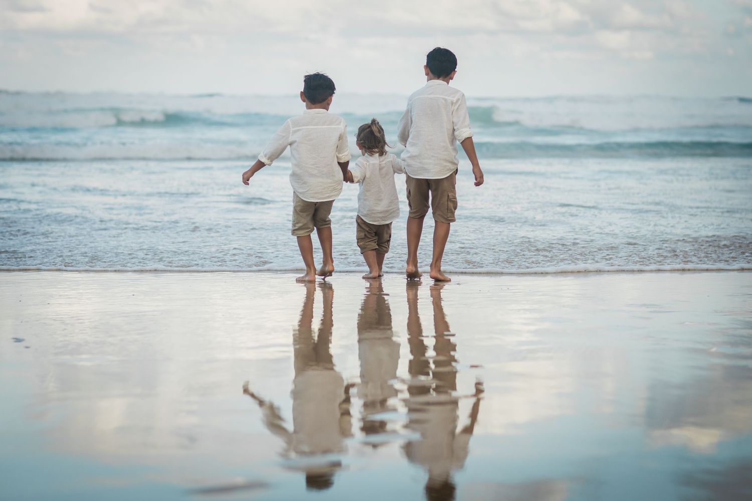 Family walking together in shallow ocean waves at sunset.Gold Coast candid family photographer.
