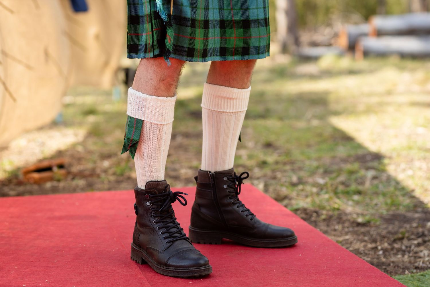 Close-up of formal footwear and traditional Scottish tartan kilt at an outdoor event.