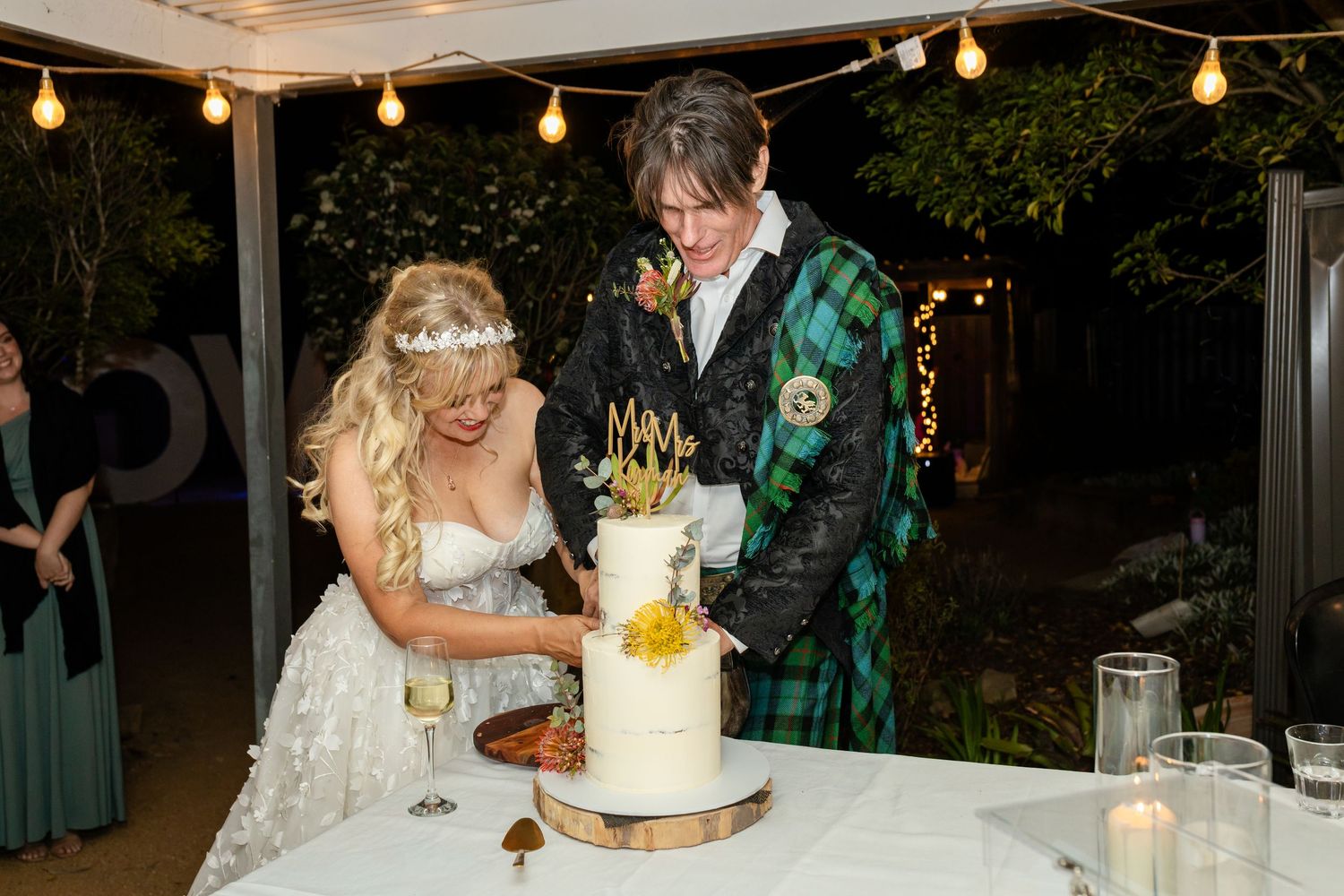 Outdoor wedding reception space decorated with string lights and cake display.