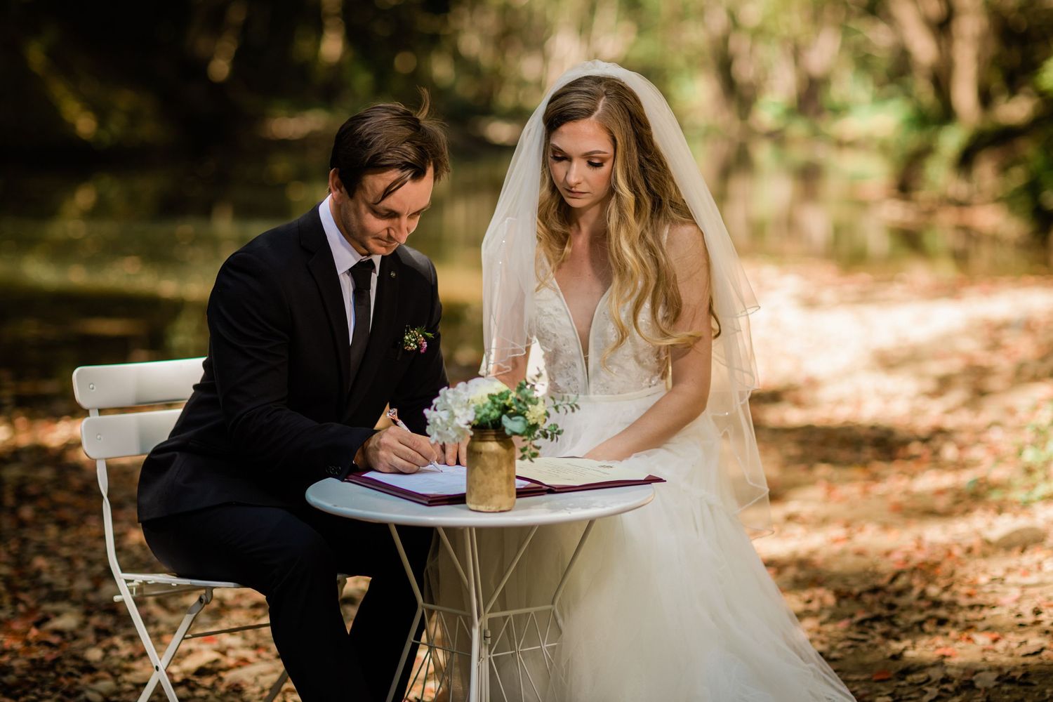 Couple signing marriage documents at small table during outdoor forest wedding.Currumbin Valley wedding photography Gold Coast
