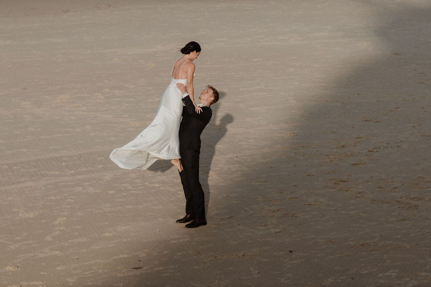 Wedding couple performing romantic dance moves on empty beach at sunset.