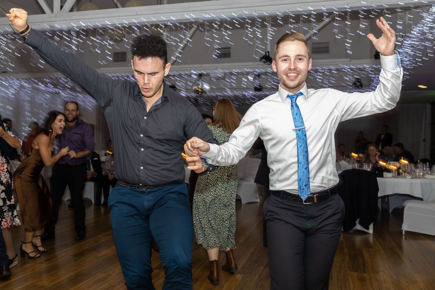 People dancing and celebrating at a wedding reception on a dance floor with festive lighting and decor.