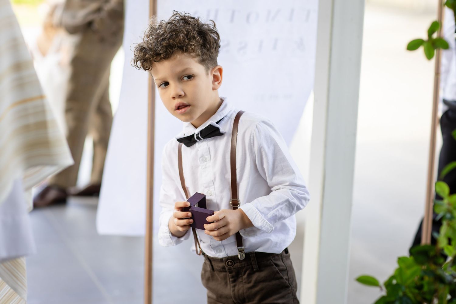 A young ring bearer in a white dress shirt holds a pillow during a wedding ceremony.