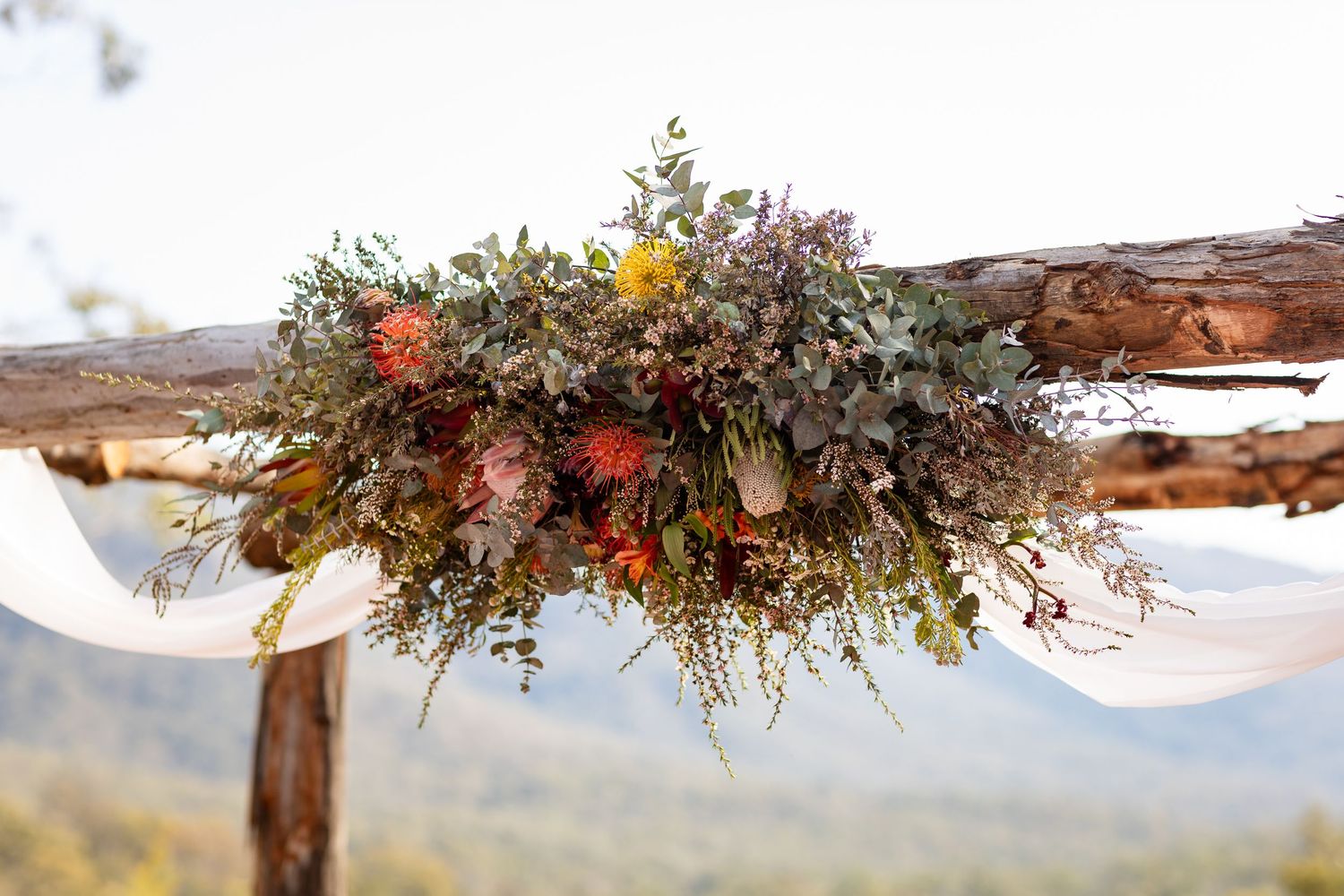 Rustic wooden arch decorated with dried flowers and greenery in an outdoor setting.