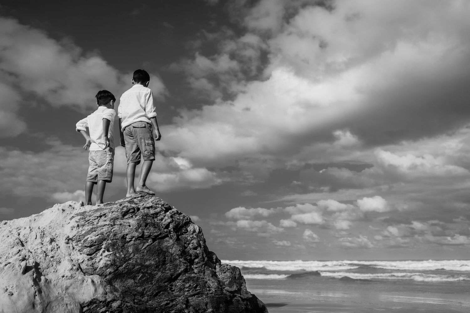 Silhouetted figures standing on rocky outcrop against dramatic cloudy sky.Gold Coast candid family photographer.
