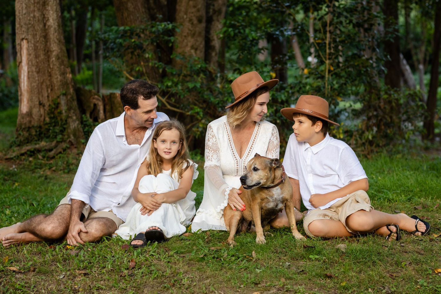 Family in white clothing sits on grass with their dog in a forest setting.Cabarita headland