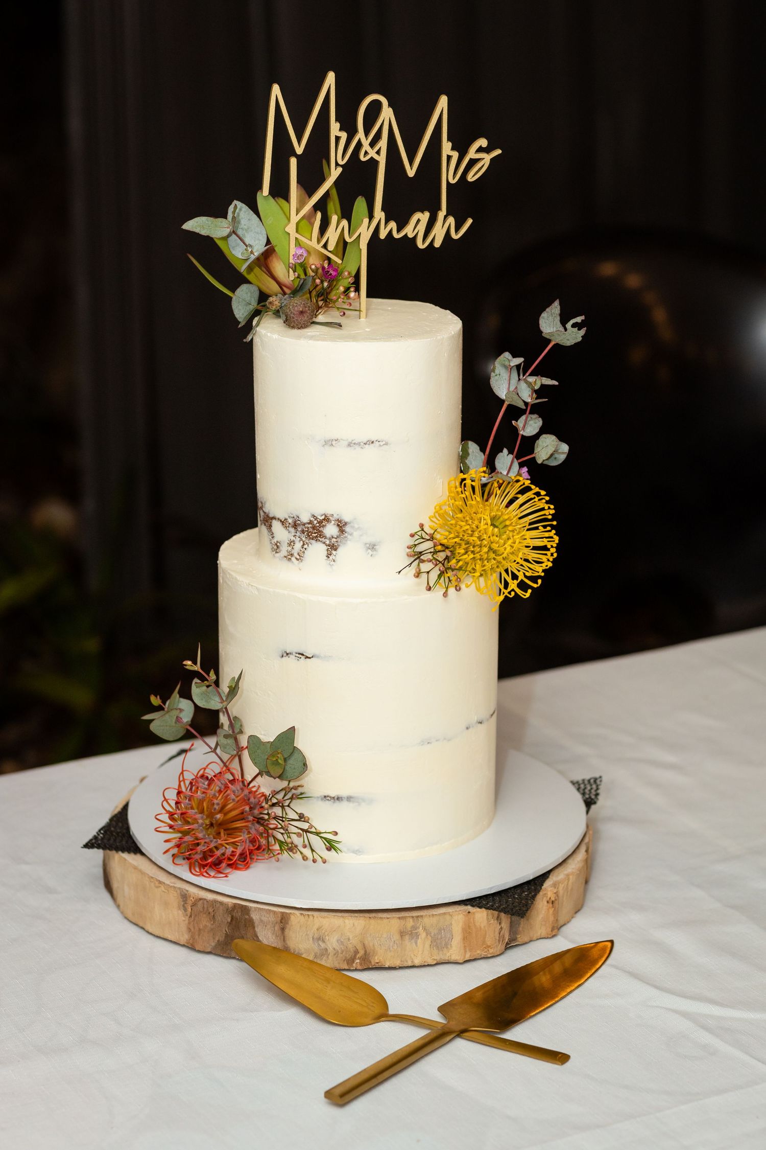Elegant white wedding cake with floral decorations and gold accents displayed on a wooden cake stand.